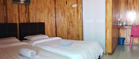 Habitación de hotel con paneles de madera, una cama con ropa blanca, un cuadro de flores, una puerta blanca y una pequeña zona de kitchenette.