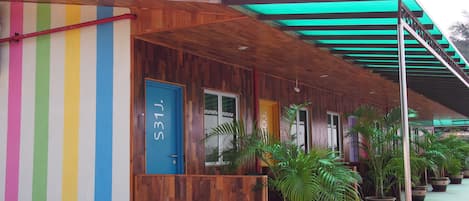 A hotel with a colorful facade, wooden exterior, and a covered outdoor area with potted plants.