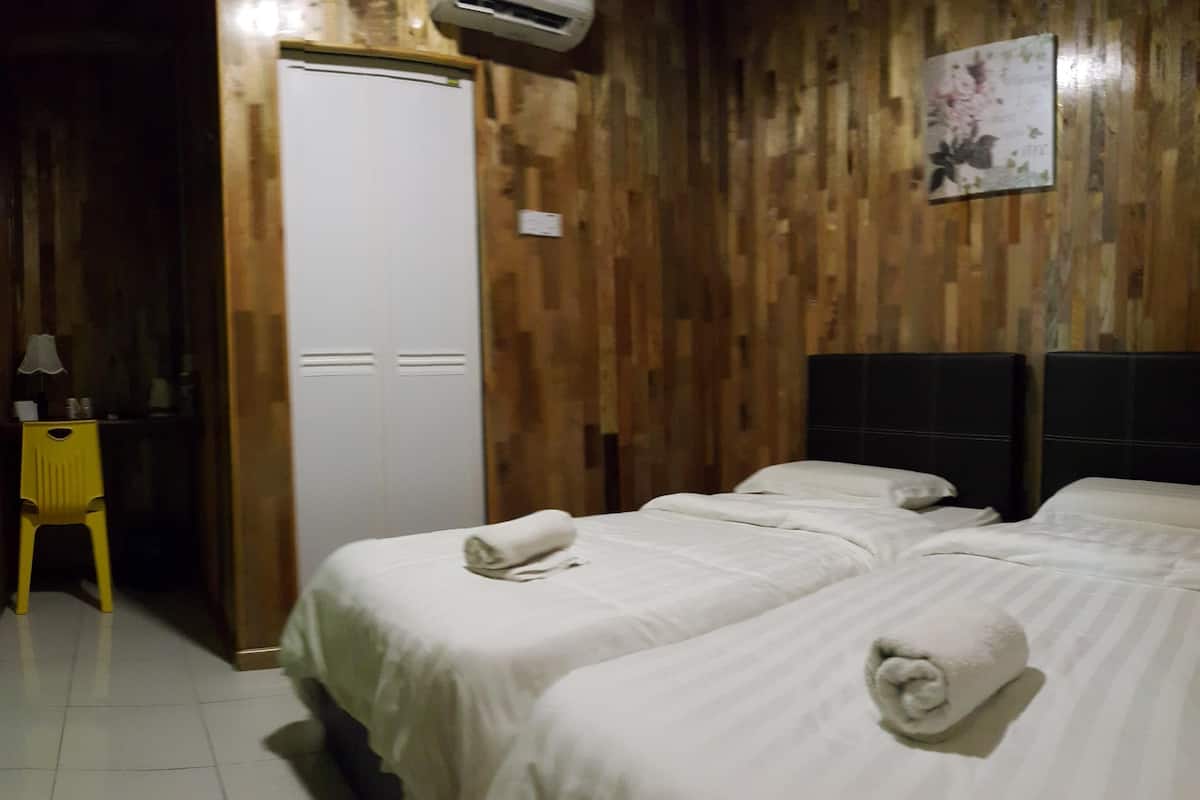 A hotel room with two beds, a wooden wall, a white door, and a small table with a lamp.