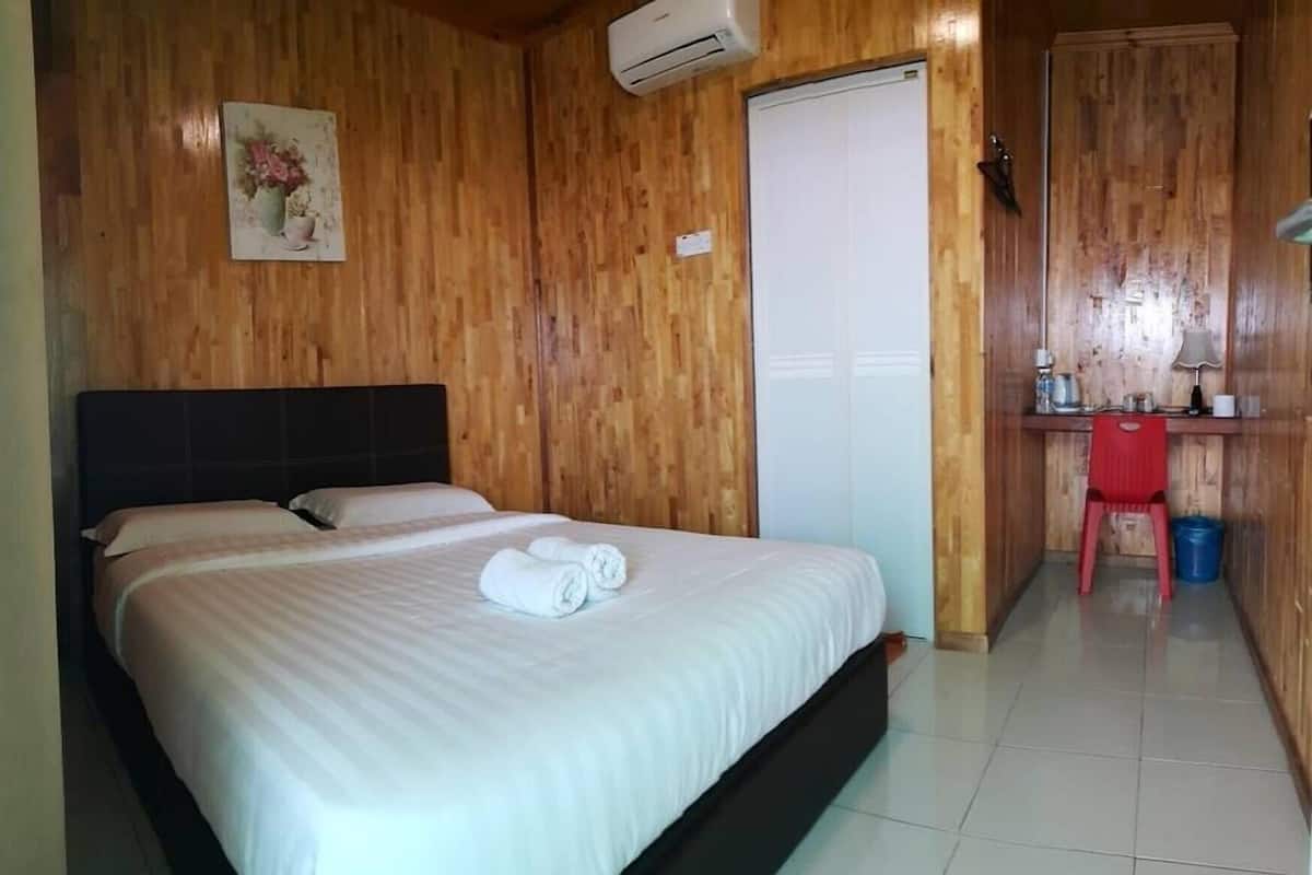 A bedroom with a bed, a desk with a chair, and an air conditioning unit.