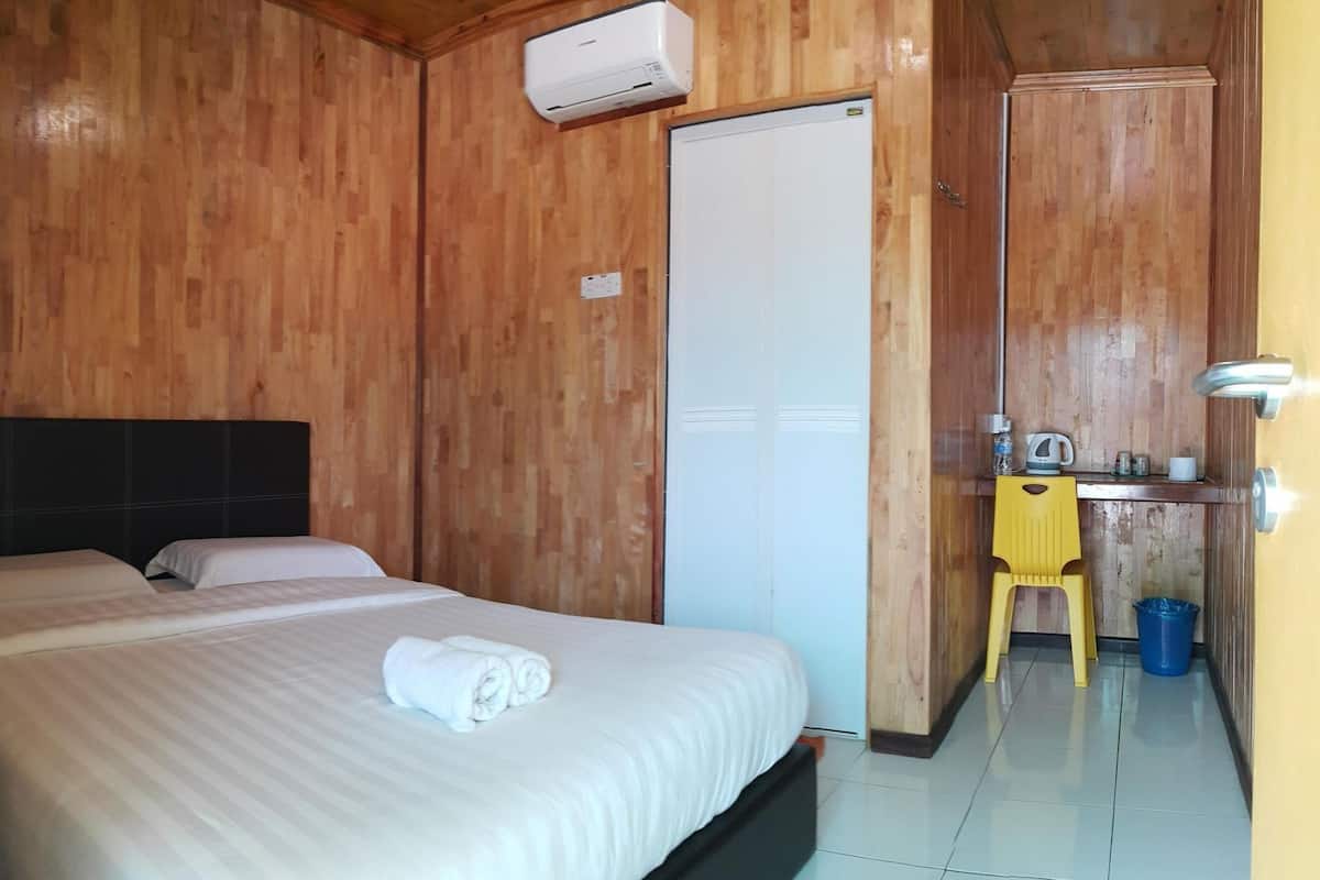 A wooden room with a bed, a small desk, a chair, and a door.