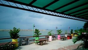 A seaside patio with tables and chairs, a railing, and potted plants. - Mabohai Resort Klebang (Malacca City)