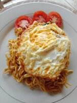 Un plato con fideos, un huevo frito y rodajas de tomate.