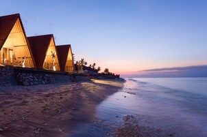 Una propiedad frente a la playa con cabañas de techo triangular de madera, un muro de piedra y un mar tranquilo.