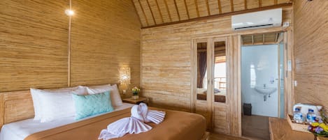 Una habitación de madera con una cama, una mesita de noche, un baño con lavamanos y un equipo de aire acondicionado.