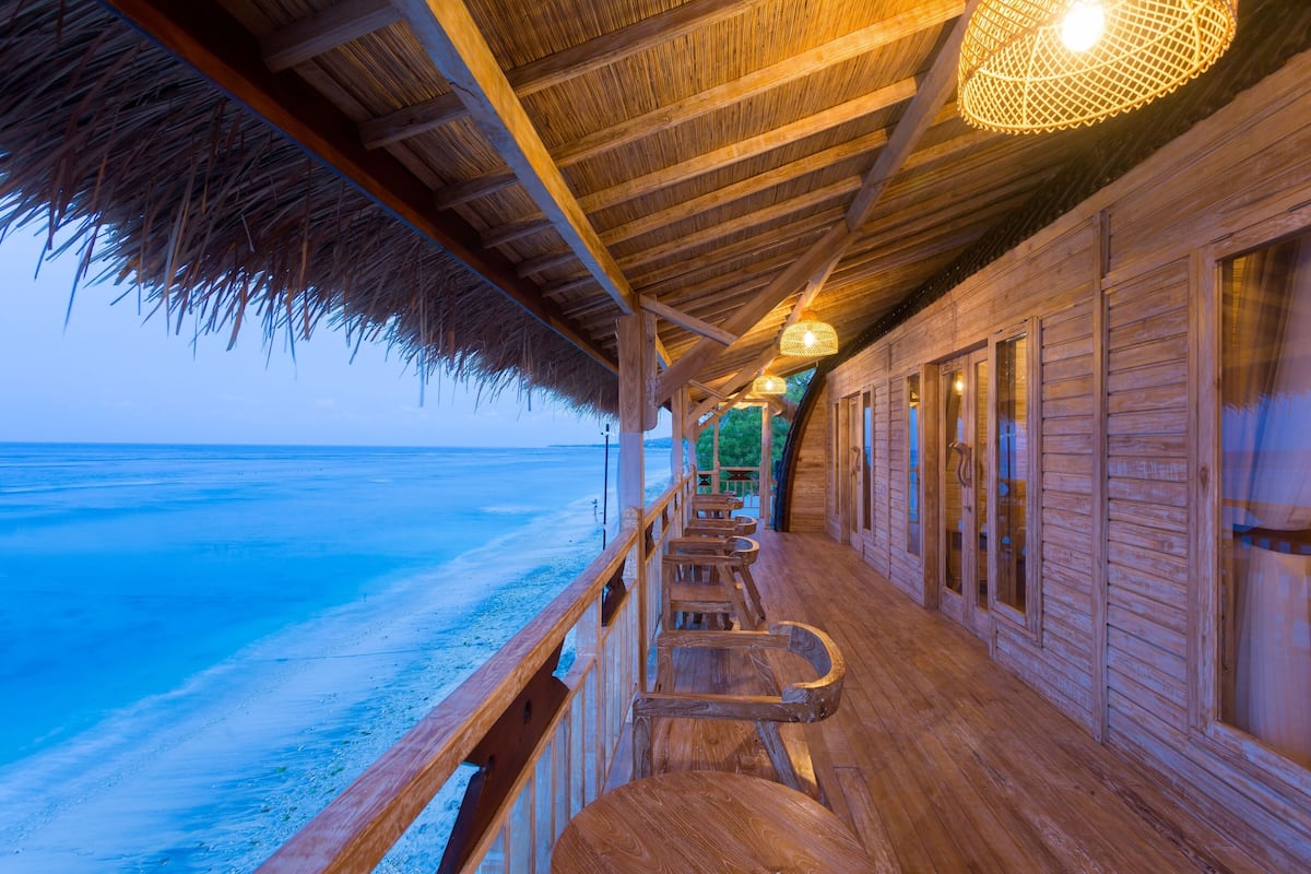 A wooden deck with a thatched roof overlooking a beach.