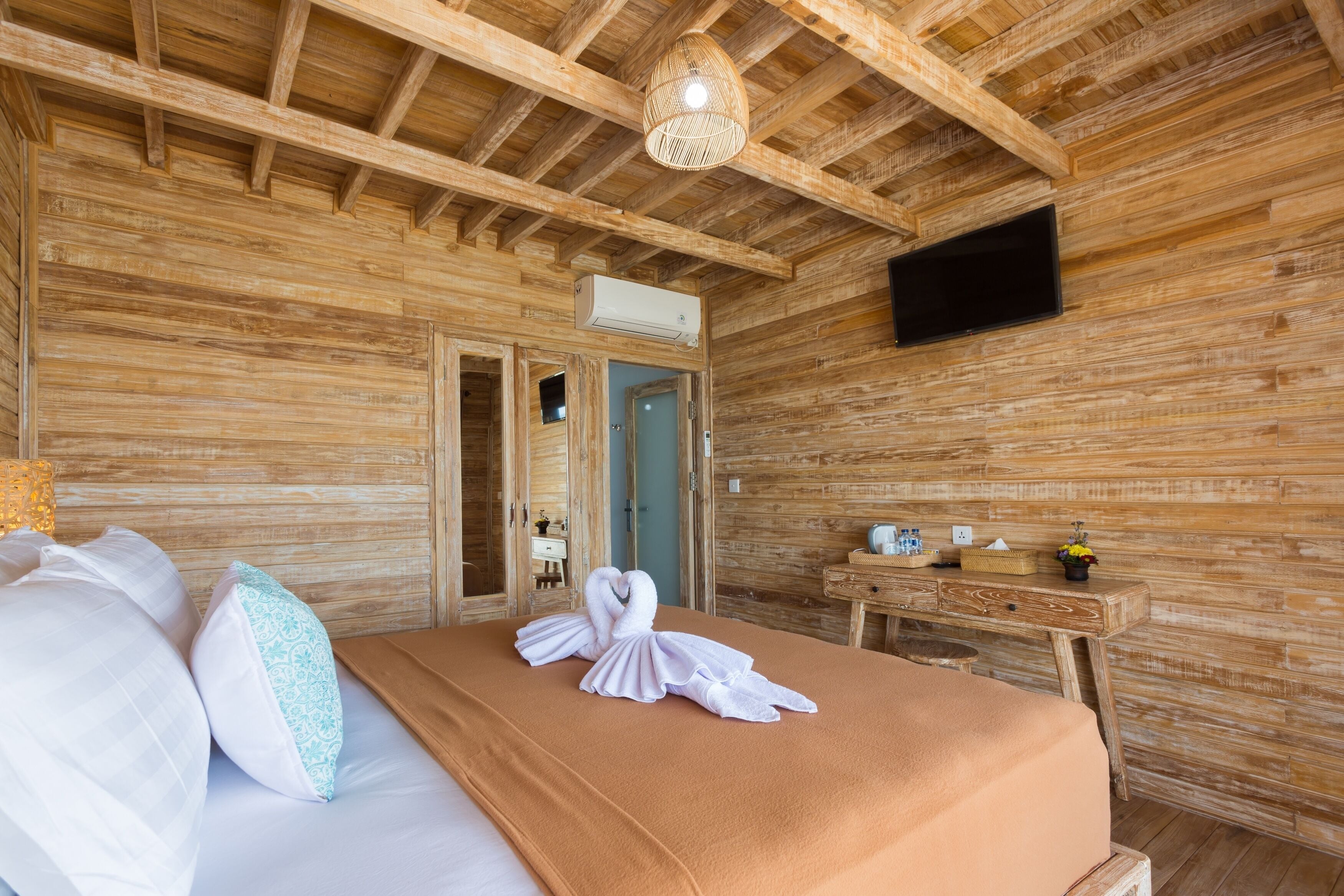 Una habitación tipo cabaña de madera con una cama, un aparador de madera, un televisor de pantalla plana en la pared y una lámpara de techo tejida.