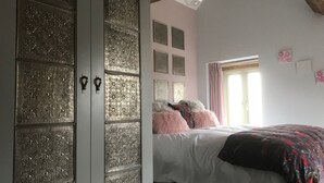 A bedroom with a large wardrobe, a bed with pink and white bedding, and a window with curtains.