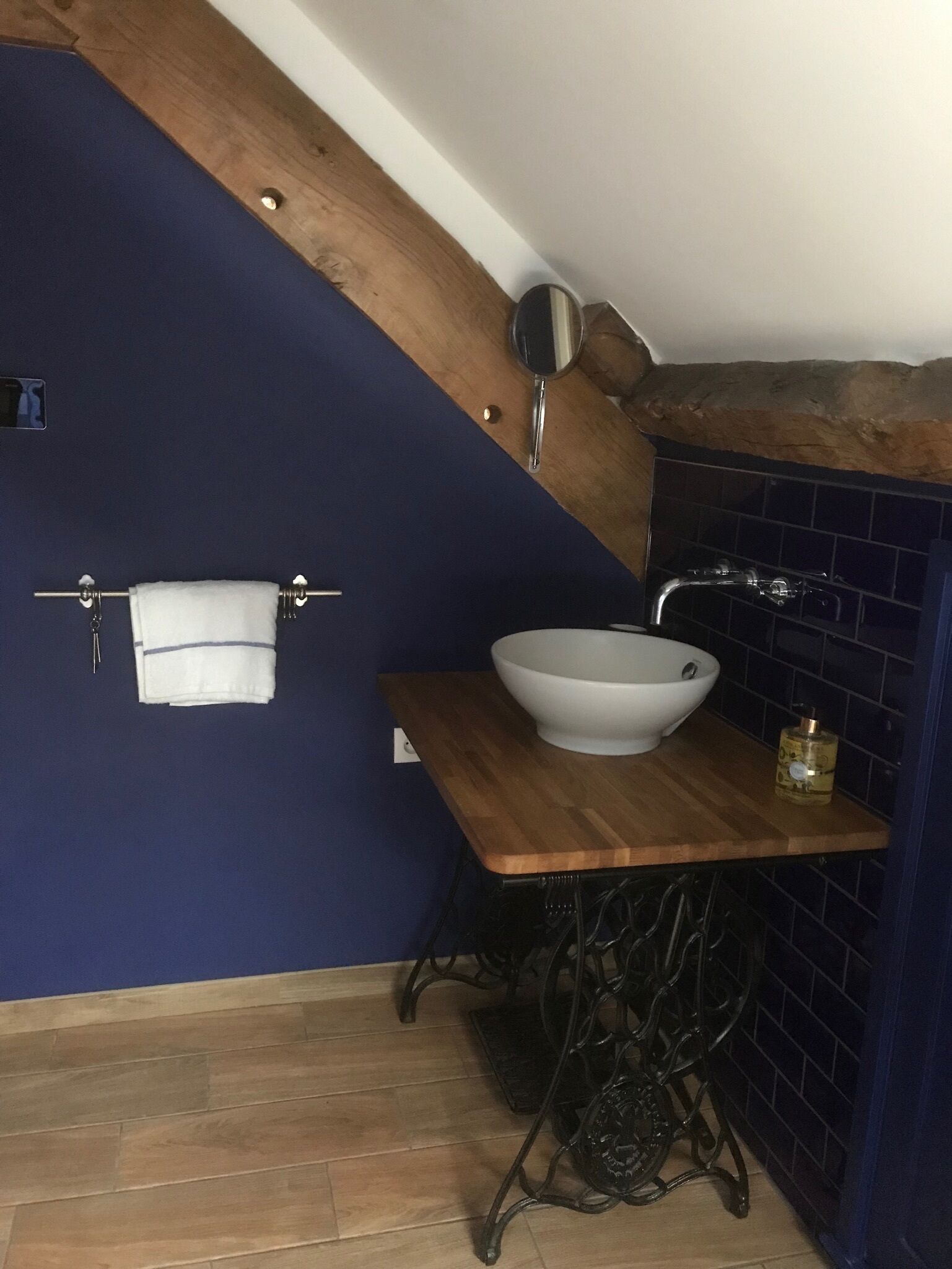 Ein Badezimmer mit einem Holzlager, einem weißen Waschbecken und einem blau gefliesten Duschbereich.