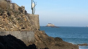 A coastal scene with a rocky cliff, a lone tree, and a distant island with a building.