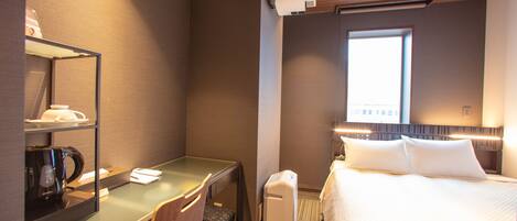 Ein Hotelzimmer mit einem Bett, einem Schreibtisch mit Computer, einem Sessel, einer Kaffeemaschine und einem Fenster.