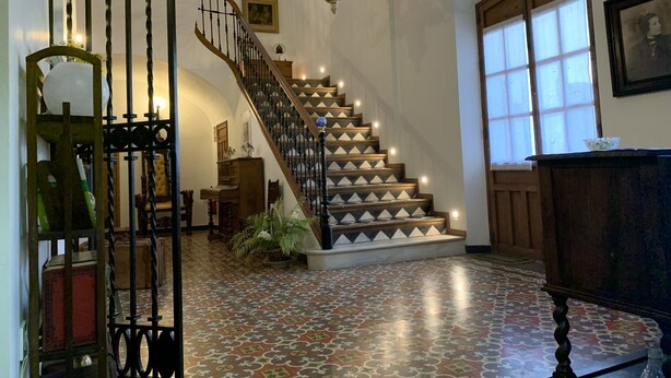 A staircase with a patterned floor, a chandelier, and a wooden door with a window.
