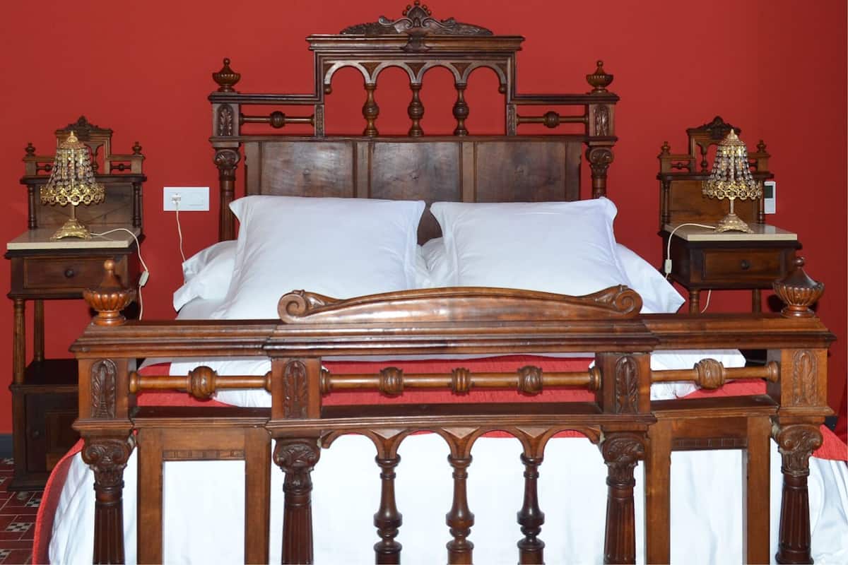 A wooden bed with a red headboard and footboard, flanked by two bedside tables with lamps.