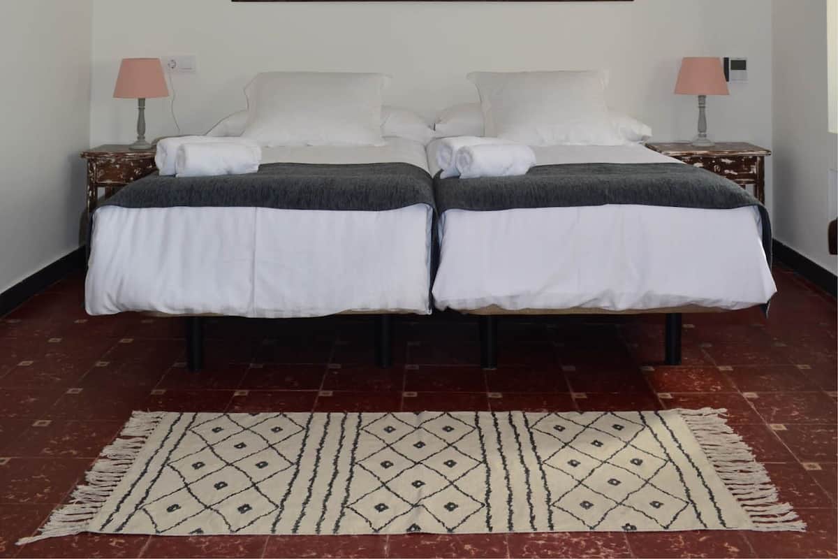 A double bed with white bedding and a dark headboard, two bedside tables with lamps, and a patterned rug on a tiled floor.