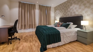 A bedroom with a bed, a desk, a chair, a nightstand, and curtains. - Trondheim Leilighetshotell (Trondheim)