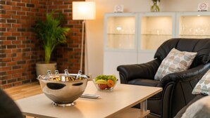 A modern living room with a brick wall, a black leather sofa, a table with a bowl of fruit, and a lamp. - Trondheim Leilighetshotell (Trondheim)