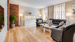 A living room with a brick wall, wooden flooring, two black leather sofas, a white coffee table, and a side table with a lamp. - Trondheim Leilighetshotell (Trondheim)