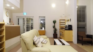 A reception area with a sofa, a coffee machine, a plant, and a counter with a sign. - Family Lodge Hatagoya Tsukuba (Tsukuba)