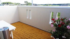 A balcony with a wooden floor, white walls, and a potted plant with flowers. - Family Lodge Hatagoya Tsukuba (Tsukuba)