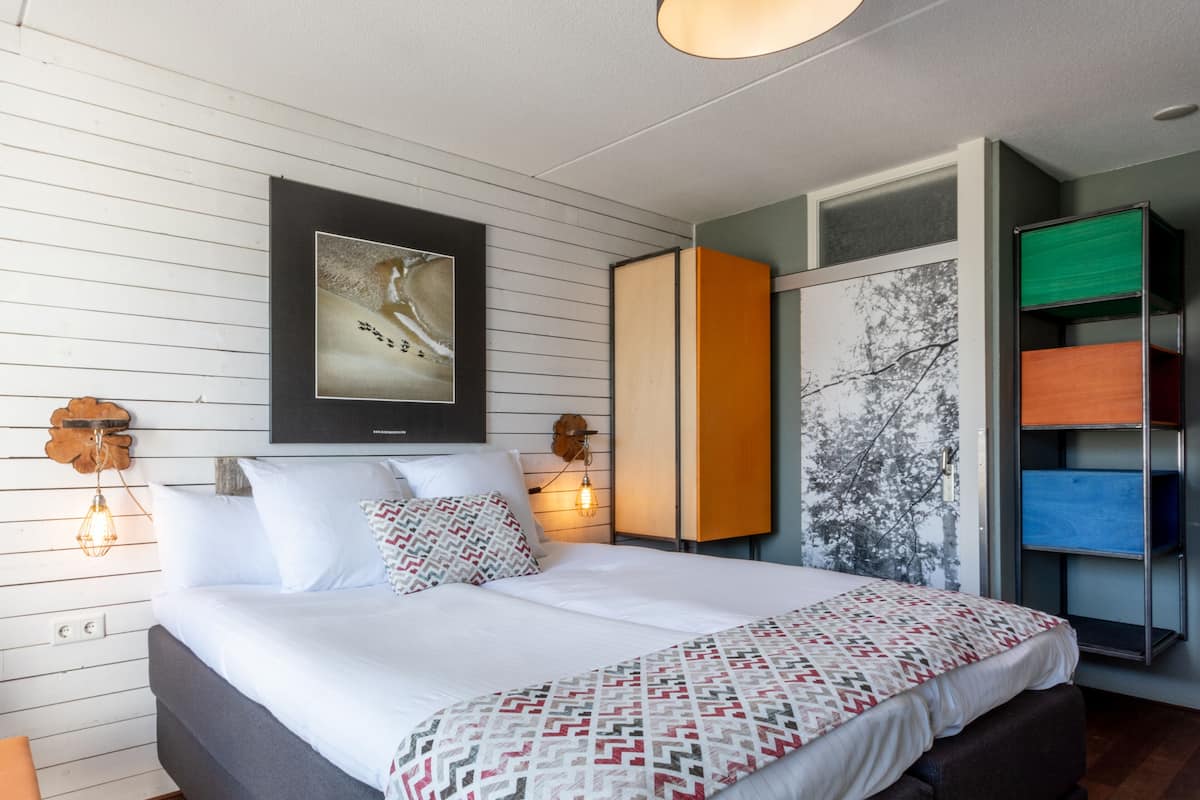 A modern bedroom with a large bed, a framed picture on the wall, and a wardrobe with multiple compartments.