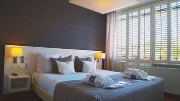 A hotel room with a large bed, two bedside lamps, a nightstand, and a window with blinds.