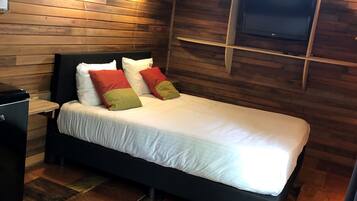 A wooden-paneled room with a bed, a TV mounted on the wall, and a small table.