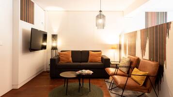 A modern living room with a black sofa, a brown leather chair, a small round table, and a hanging light fixture.