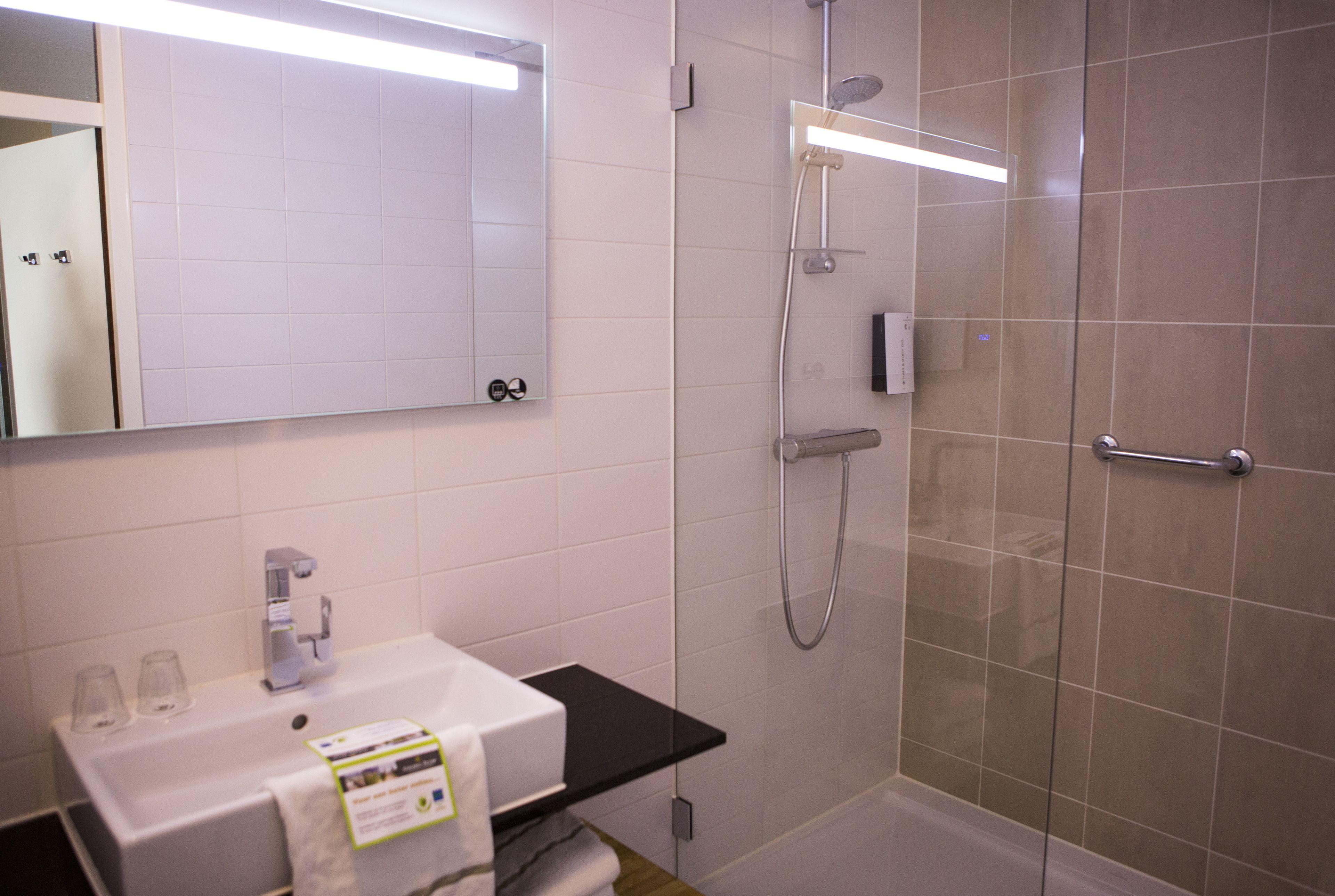 Une salle de bain moderne avec un lavabo blanc, un miroir, une douche avec une porte en verre et un plan de toilette noir.