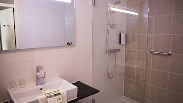 Une salle de bain moderne avec un lavabo blanc, un miroir, une douche avec une porte en verre et un plan de toilette noir.
