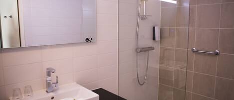 Un baño moderno con lavamanos blanco, espejo, ducha con puerta de cristal y encimera negra.