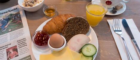 Ein Frühstücksteller mit Croissant, Roggenbrot, Käse, Schinken, Ei und Gurkenscheiben.