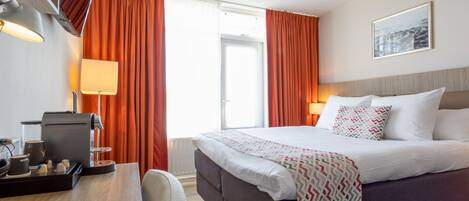 Une chambre d’hôtel avec un lit, un bureau doté d’une machine à café et une fenêtre avec des rideaux.