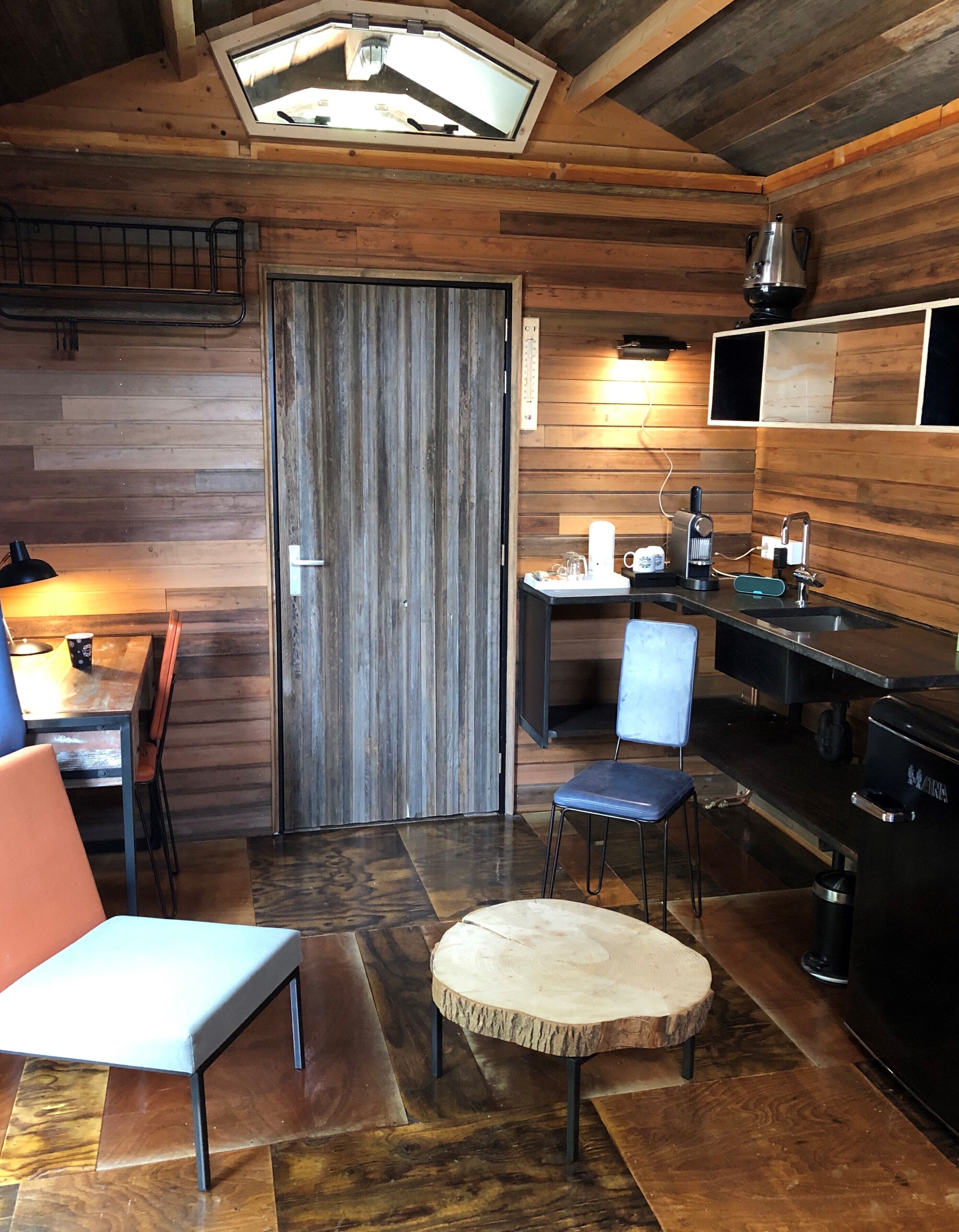 A cozy cabin-style room with a wooden interior, a kitchenette, a dining area with a table and chairs, and a large window.