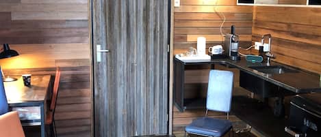 Een gezellig houten kamer in chaletstijl, met een kitchenette, een eethoek met tafel en stoelen, en een groot raam.