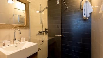 Un baño moderno con lavamanos blanco, ducha con cerramiento de vidrio y paredes de azulejos oscuros.