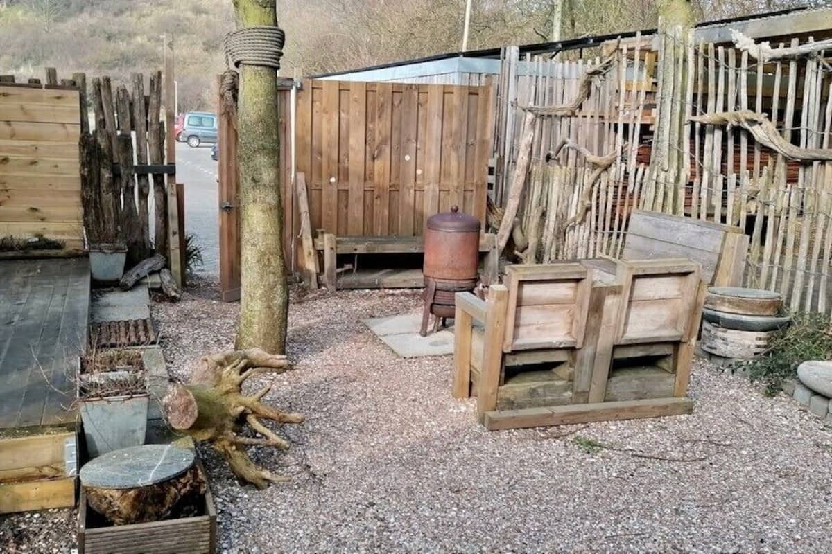 A rustic outdoor area with a wooden deck, a rustic wooden fence, and various wooden furniture pieces.