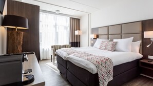 Ein modernes Hotelzimmer mit einem großen Bett, einem Schreibtisch mit Kaffeemaschine und einem an der Wand befestigten Fernseher.
