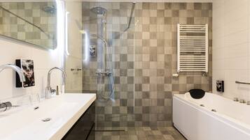 Un baño moderno con una bañera grande, una zona de ducha independiente con puerta de vidrio y un tocador con espejo y dos lavamanos.