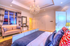 A bedroom with a large bed, a sofa, a chandelier, and a wardrobe.