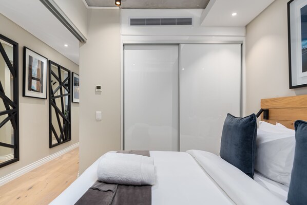 A modern hotel room with a large bed, a wooden headboard, a sliding door closet, and framed artwork on the wall. - Docklands 519 (Cape Town)