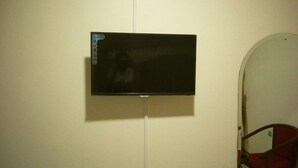 A flat-screen TV mounted on a white wall in a room with a red chair and a white door. - Prestige Hotel & Club Nyeri (Nyeri)