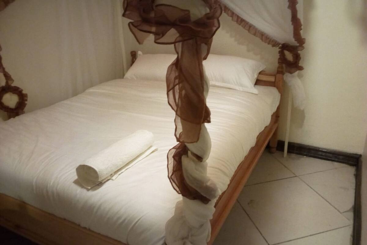 A bed with a canopy, white bedding, and a rolled towel.