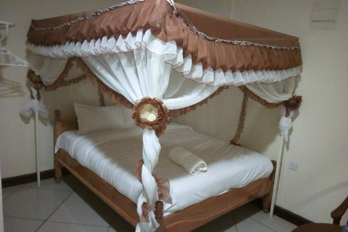 A wooden bed with a canopy, white bedding, and a decorative pillow.
