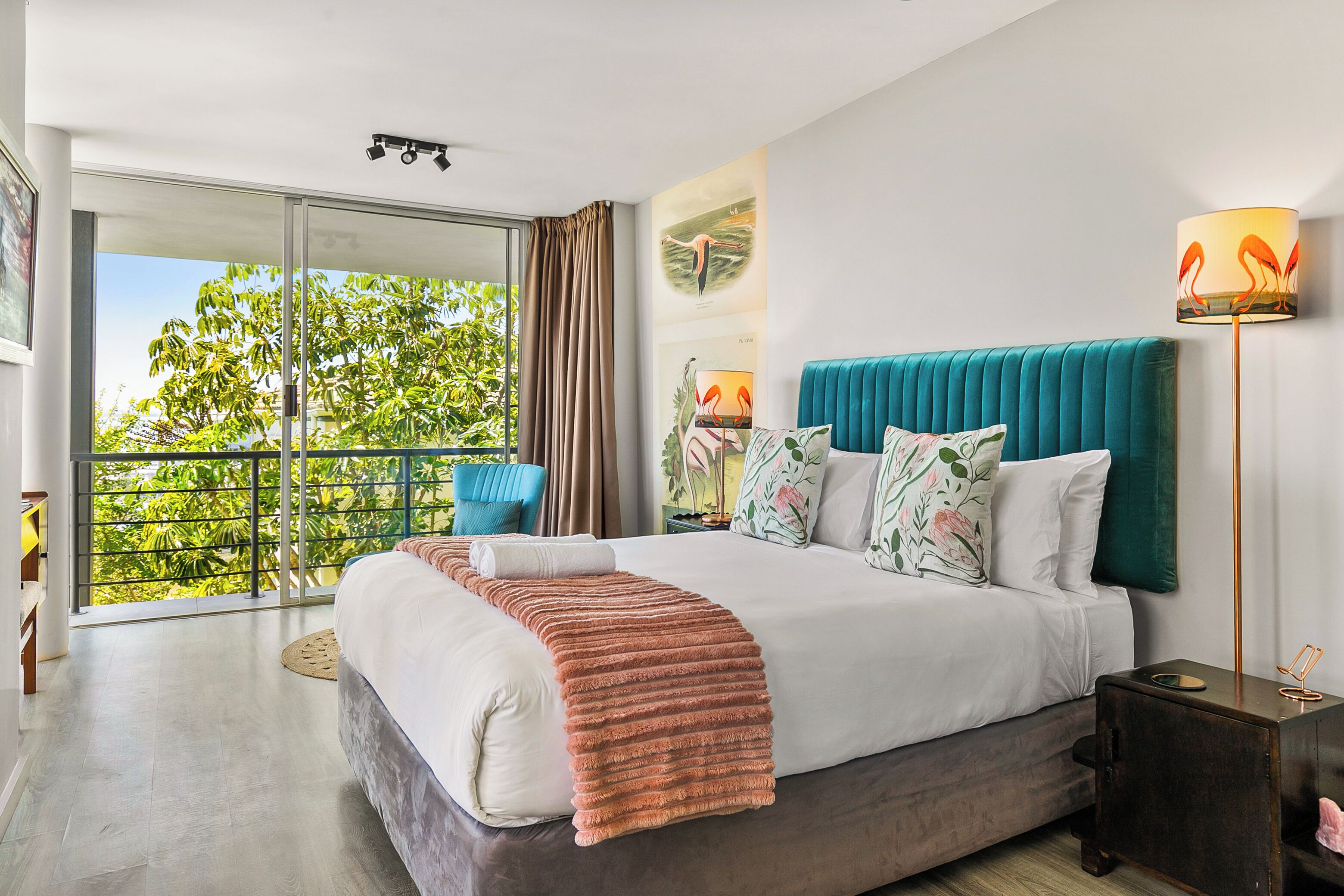 A modern bedroom with a large bed, a balcony with a view, and a floor lamp.