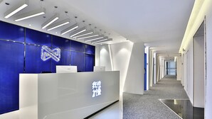 A modern reception area with a sleek reception desk, a blue accent wall, and a long corridor leading to other rooms. - Hangzhou Infinity Youth Hostel (Hangzhou)