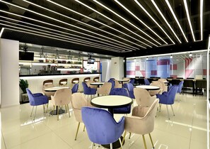 A modern cafe with a bar area, round tables, and blue chairs. - Hangzhou Infinity Youth Hostel (Hangzhou)