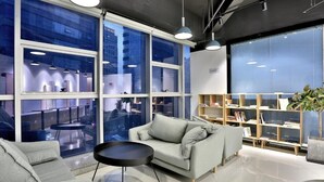 A modern office space with large windows, a sofa, a coffee table, and a bookshelf. - Hangzhou Infinity Youth Hostel (Hangzhou)