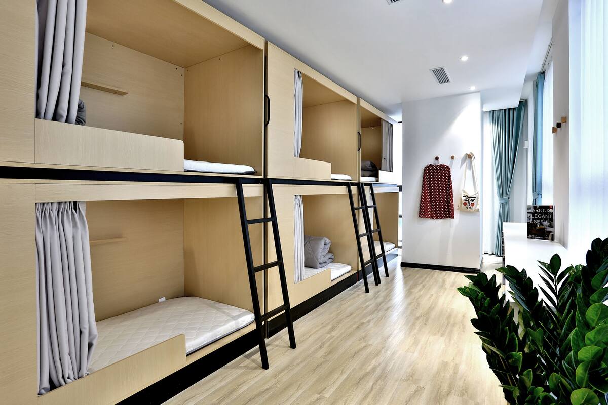 Habitación con literas, suelo de madera, una escalera y una ventana con cortinas.