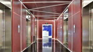 A modern elevator interior with metallic walls, a reflective floor, and a blue exit sign. - Hangzhou Infinity Youth Hostel (Hangzhou)