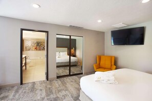 A hotel room with a bed, a chair, a TV, and a bathroom visible through a sliding door. - the riverside hotel (Boise)